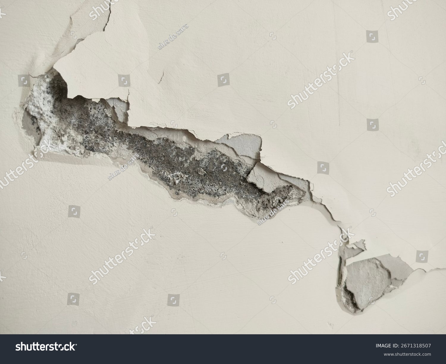 Rissige Wand mit abblätterndem Putz und freigelegtem Beton